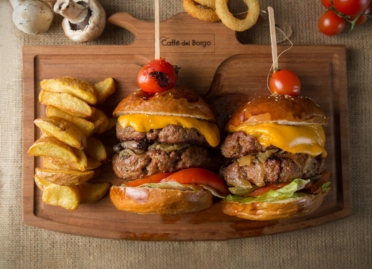 Kesme tahtası üzerinde ortadan ikiye kesilmiş büyük bir burger, üstten görünüş.