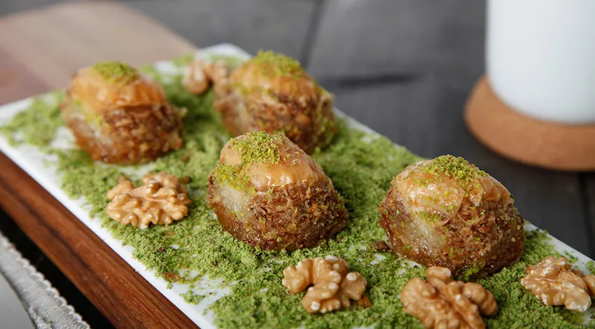 Beyaz tabakta toz fıstık üzerinde cevizli baklava.