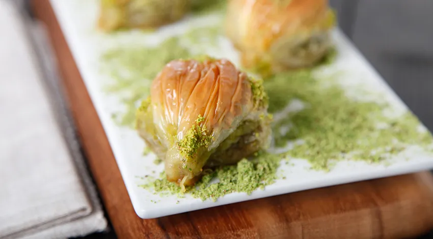 Beyaz tabak içinde fıstıklı midye baklava.