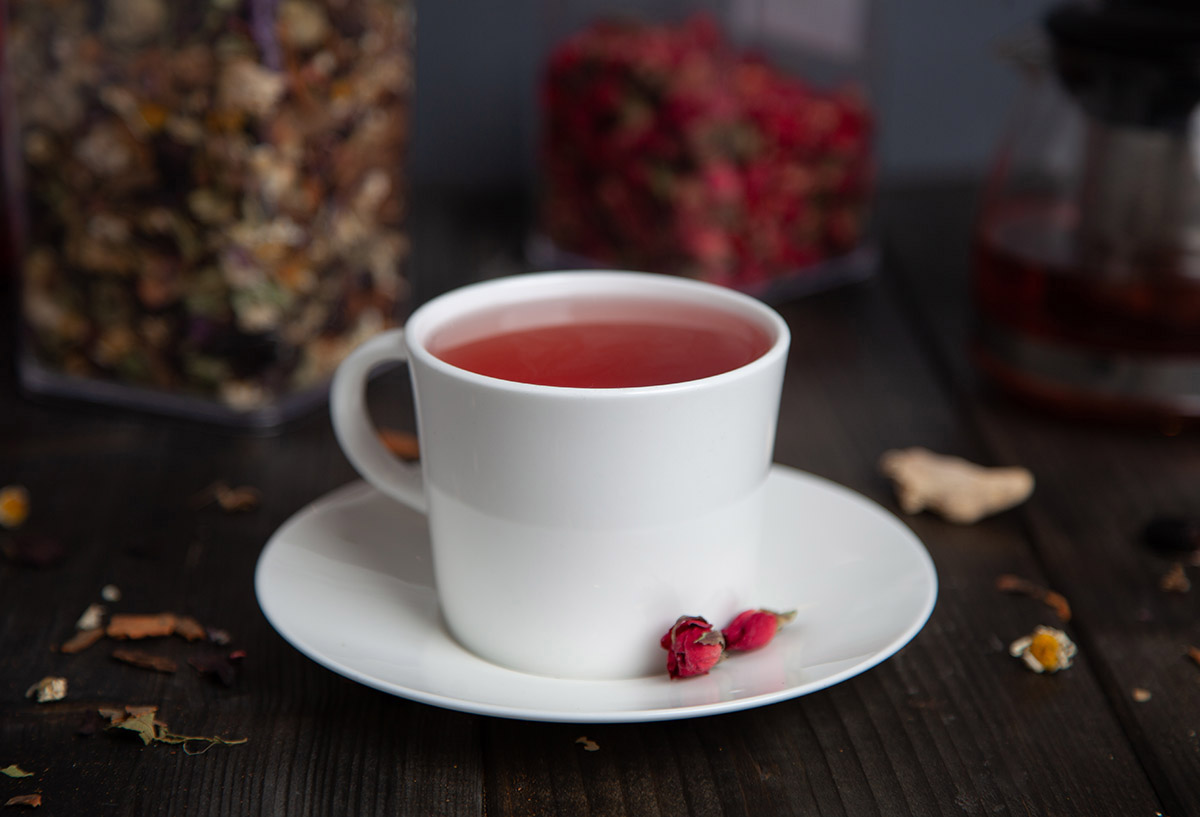 Kırmızı renkli kış çayı fincan içerisinde arka planda kavanoz içerisinde kuru kış çayı.
