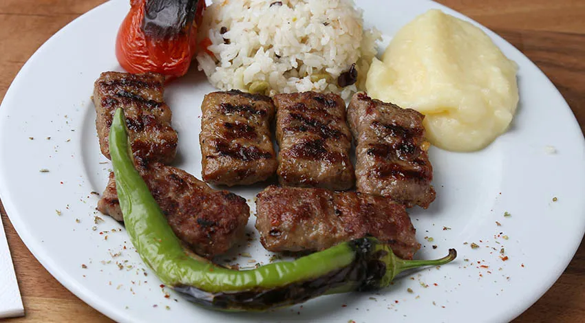 Altı adet köfte, pilav, yeşil, biber, patates püresi, domates ile servis edilmiş