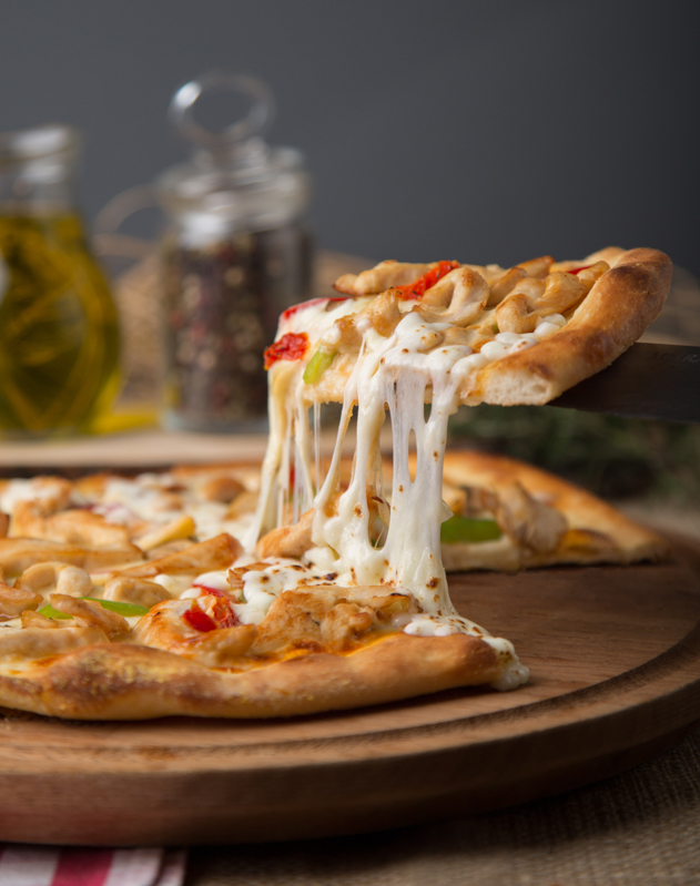 Spatula ile alınan pizza diliminden peynirler uzuyor.