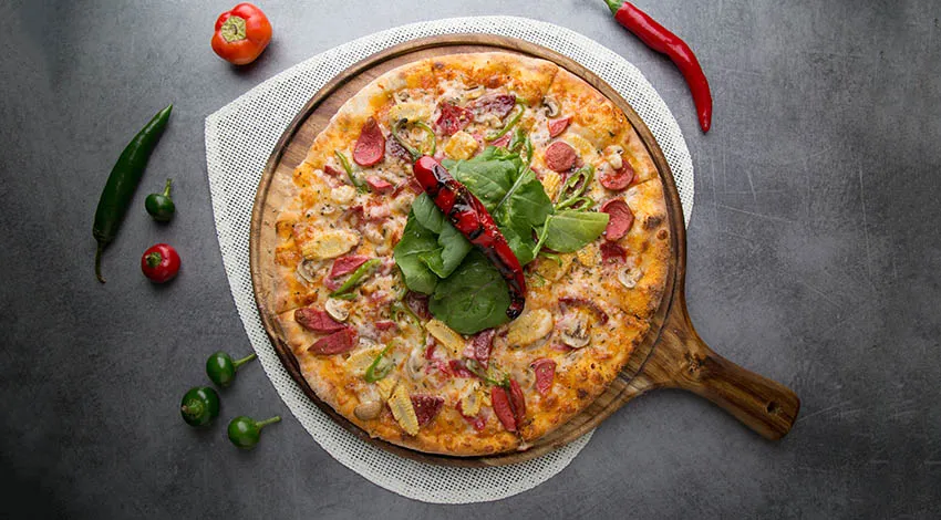 Ahşap sunum tahtasında servis edilen bir pizza üstten görünüm etrafında biber ve domatesler