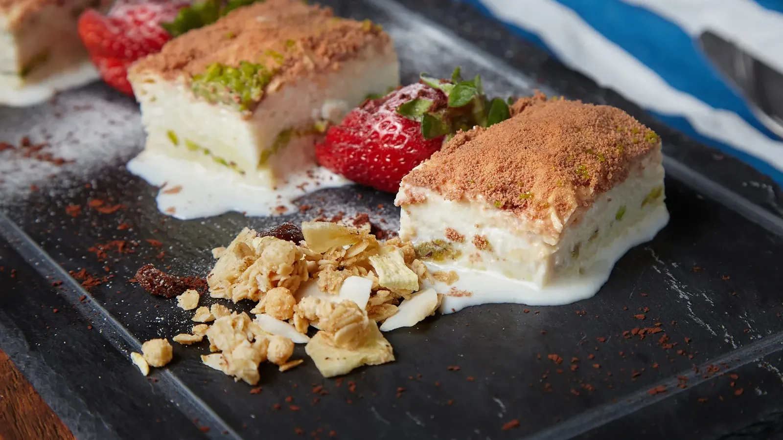 Siyah granit tabak içinde üç adet soğuk baklava ve çilekler.