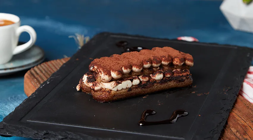 Yanında küçük bir fincan espresso olan tiramisu tatlısı.