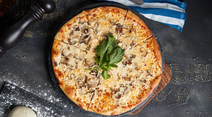 Üstten çekilmiş bir pizza fotoğrafı yanında çiğ top şeklinde hamur var.